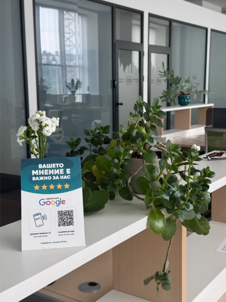 Офисен рафт с саксийни растения и табела с отзив от Google, снабдена с QR код и NFC функция, в модерно работно пространство.